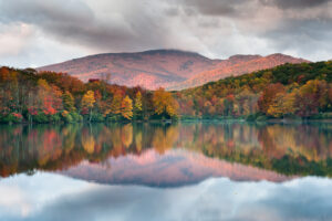 a stunning mountain lake surrounded by trees in the fall, with leaves of red, green, orange, and gold. a large mountain is in the background